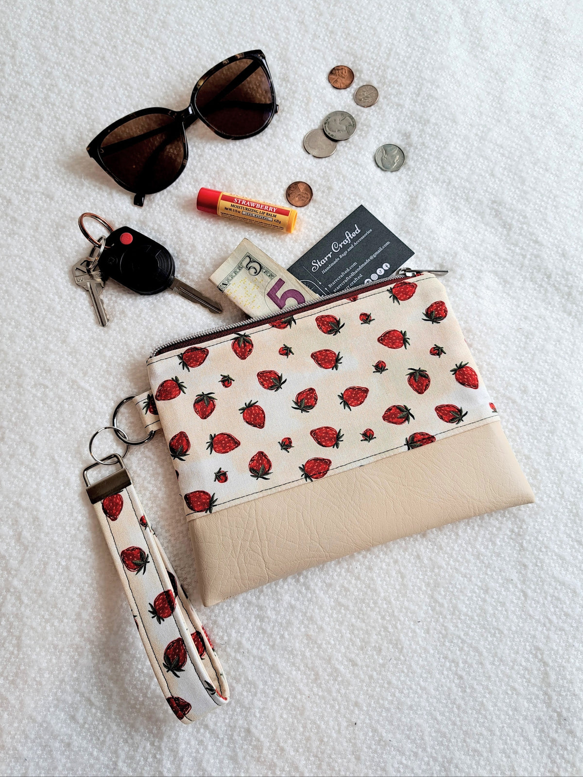 Strawberry-patterned pouch with sunglasses, keys, money, and other small items on a white surface